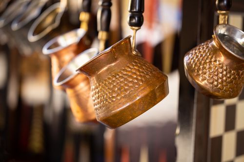 Free Close-up of traditional copper coffee pots hanging on a display rack, reflecting warm tones. Stock Photo