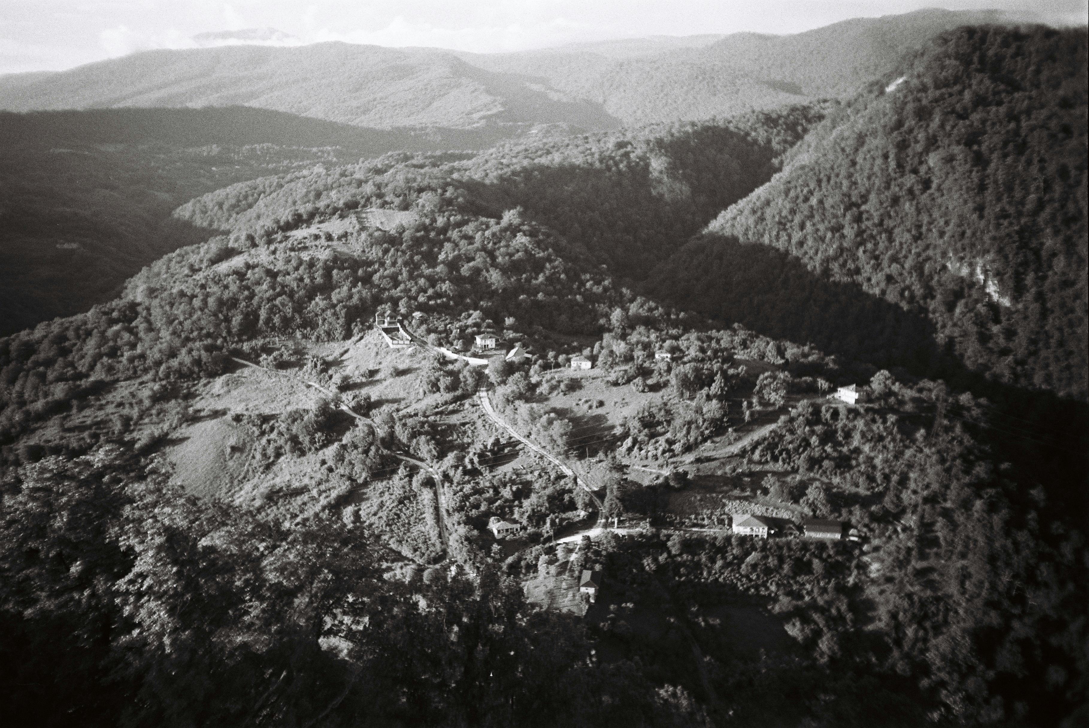 A scenic aerial view showcasing a rural village amidst forested hills in monochrome.
