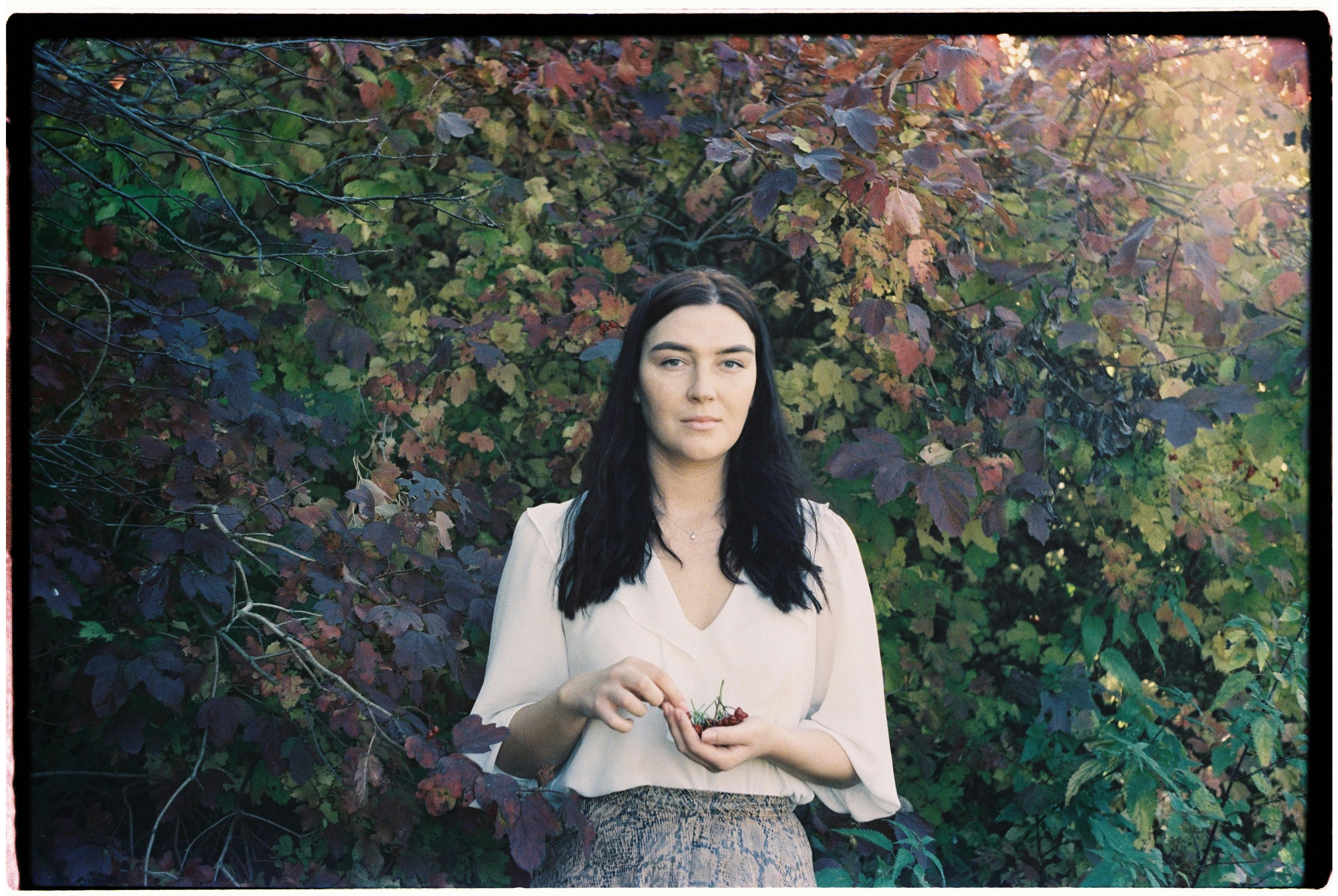 A woman stands amidst colorful autumn leaves, exuding calmness and beauty.