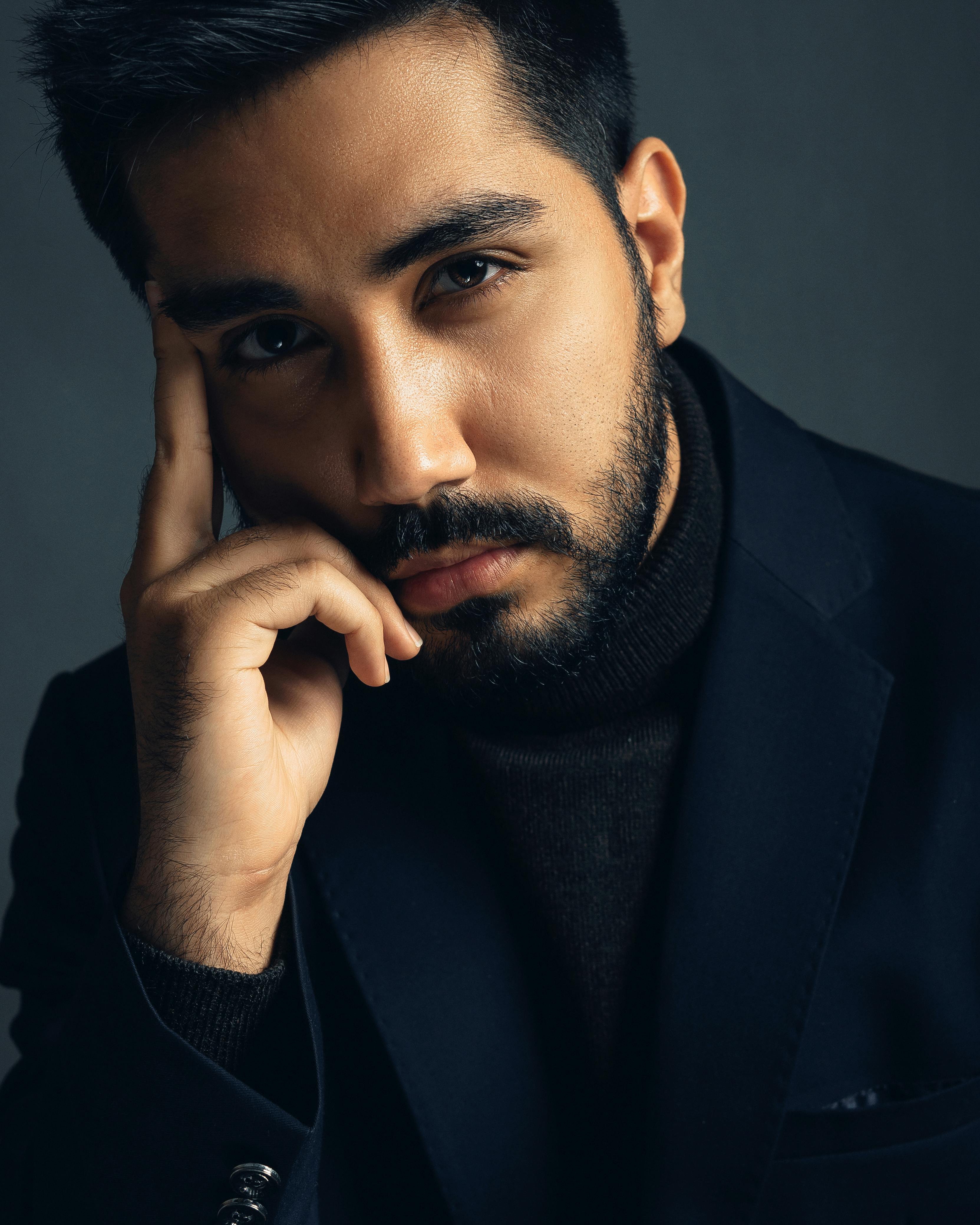 Portrait of a serious man with a beard, wearing a dark suit, striking a pensive pose.