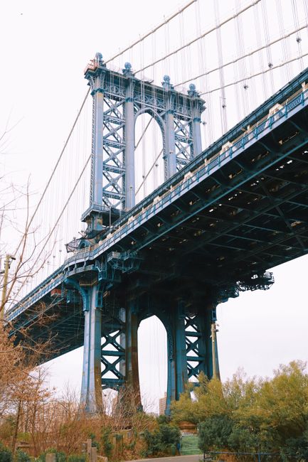 A low angle shot capturing the Manhattan Bridge, showcasing its blue steel structure amidst a clear sky.