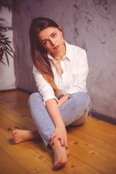 Beautiful woman with long brown hair sitting on a wooden floor indoors.