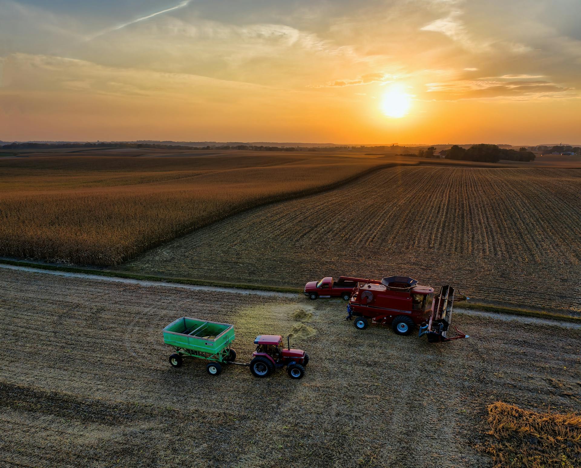 Drone shot capturing tractors and combine harvester working on a farm in Minnesota at sunset. Picturesque agricultural scene.