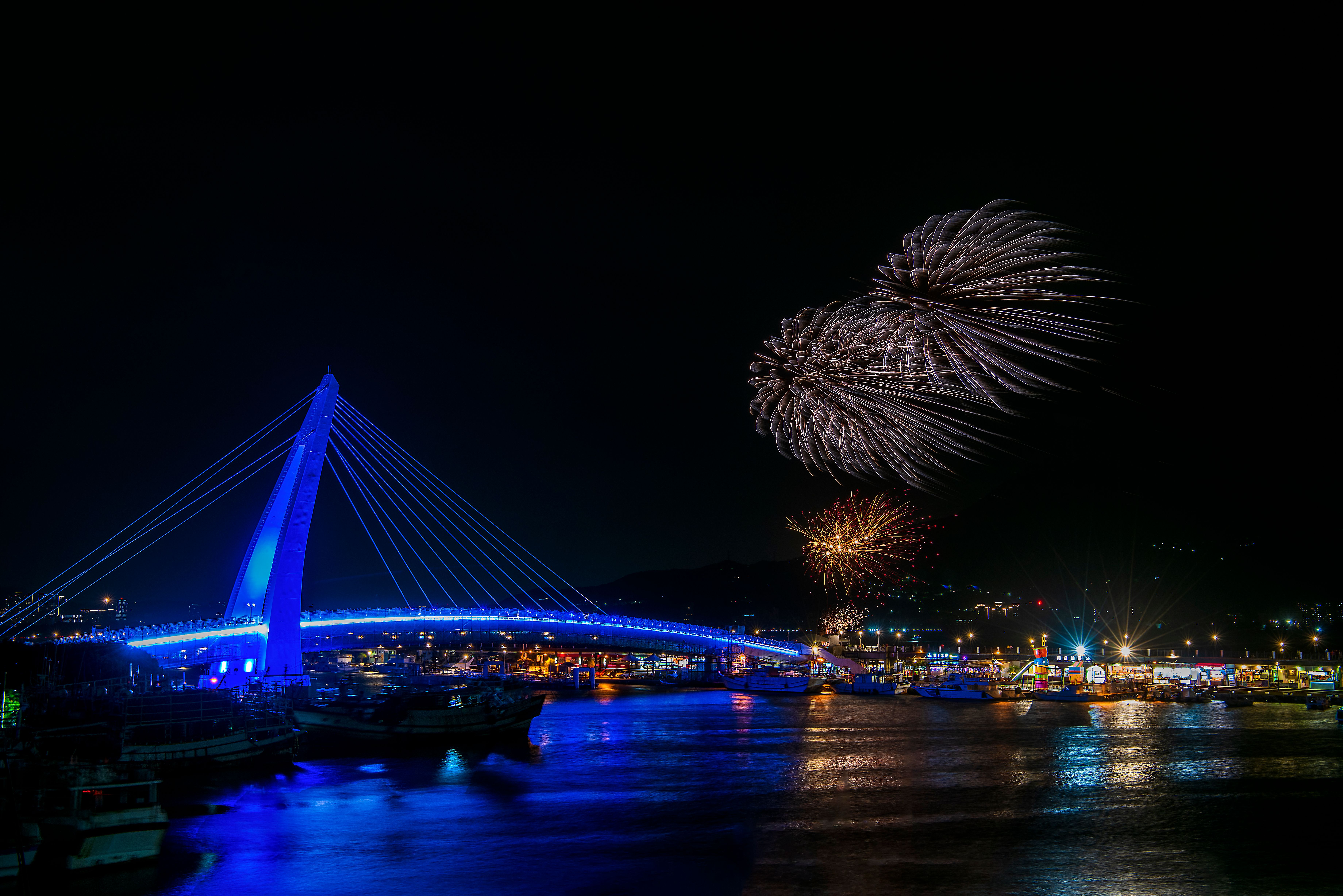 Nighttime firework spectacle over Tamsui Lovers Bridge, Taiwan, capturing vibrant colors and reflections.