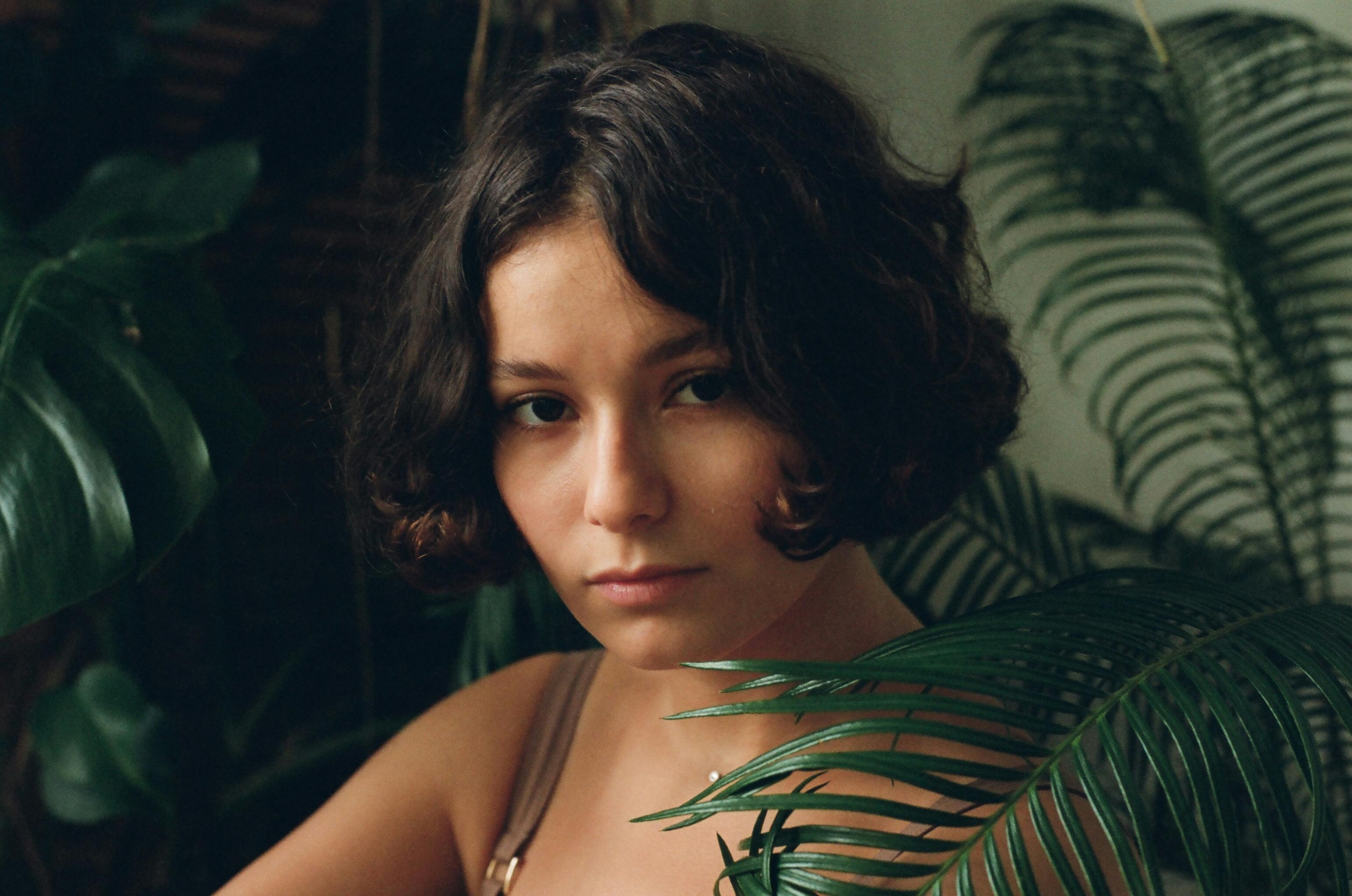 A captivating portrait of a young woman surrounded by lush green plants, conveying a serene and natural vibe.