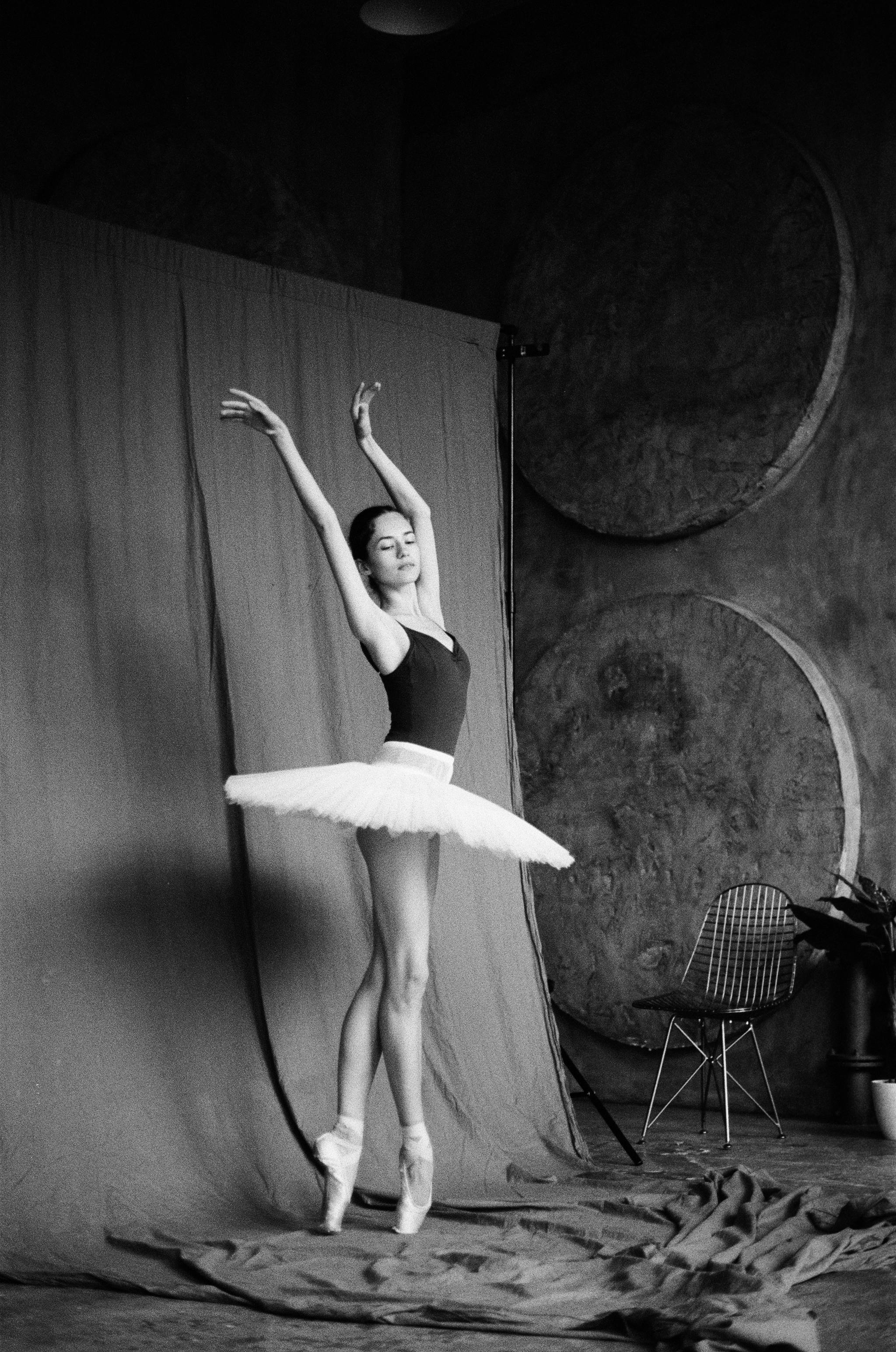 Black-and-white image of a ballet dancer in a graceful pose against a studio backdrop.