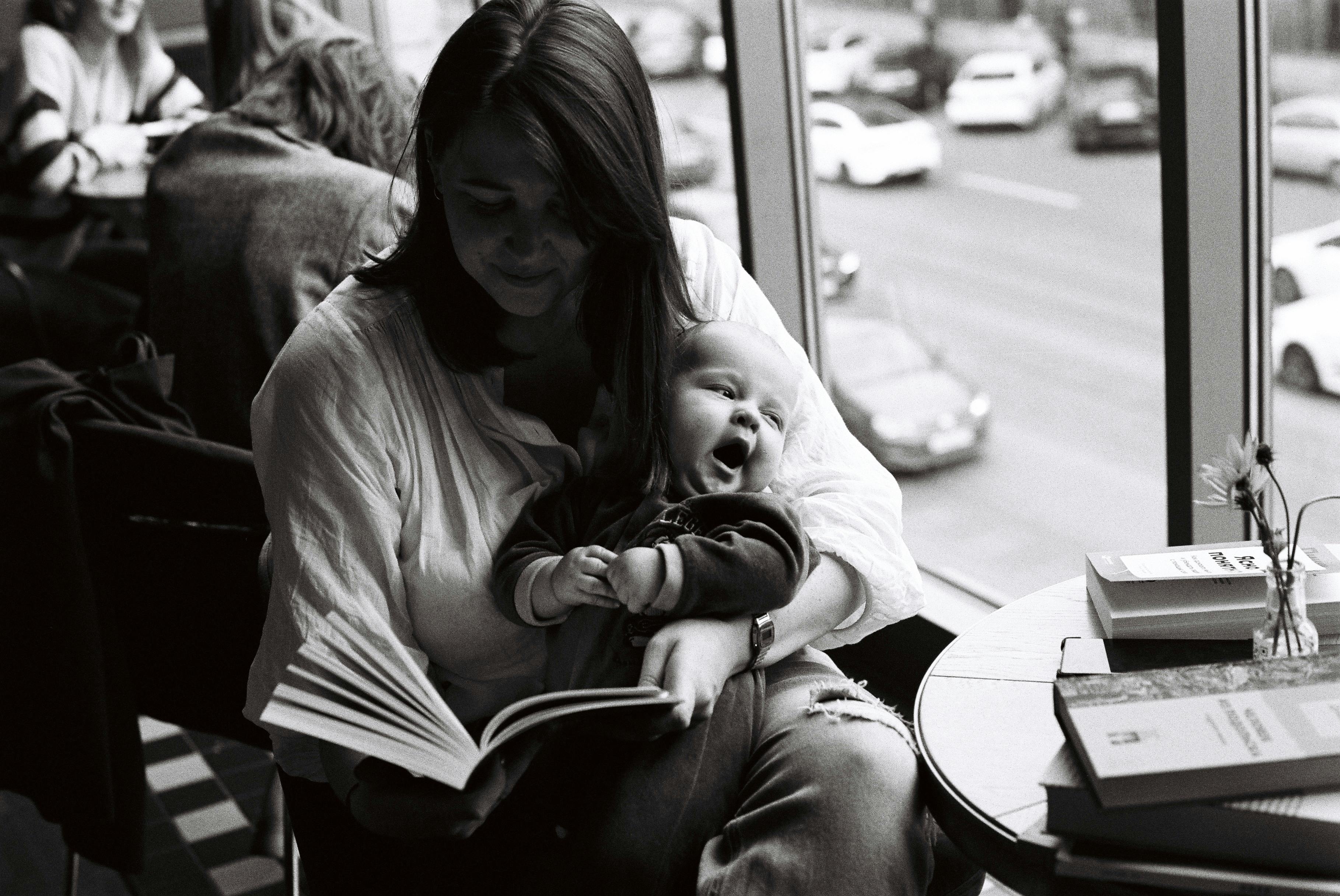 woman in long sleeve shirt carrying a baby while a reading book
