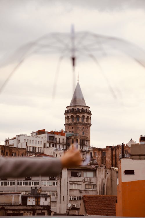 Unrecognizable Hand Holding Transparent Umbrella Before View on Tower