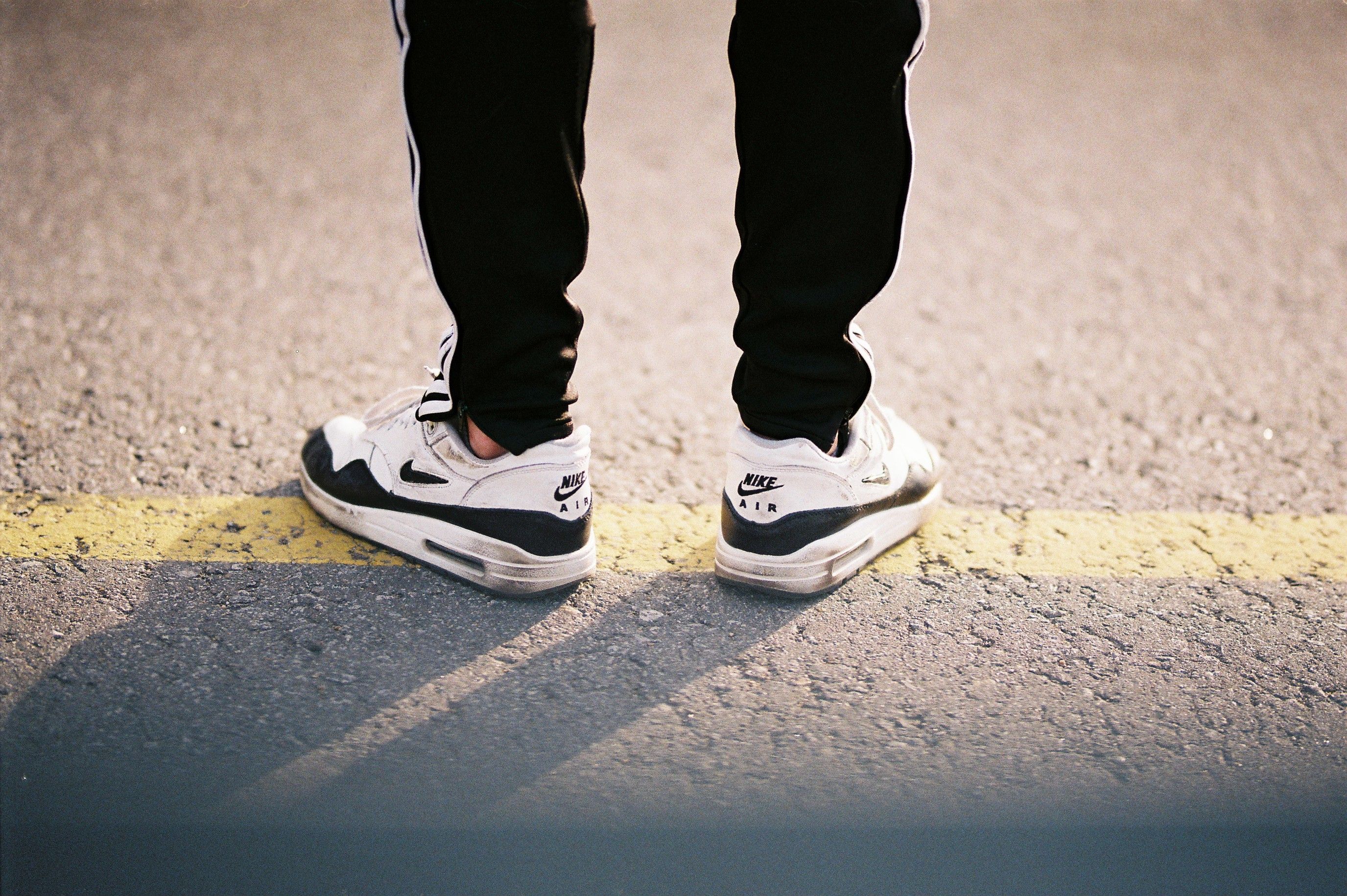 Person wearing black pants and sneakers standing on a road - close-up urban fashion