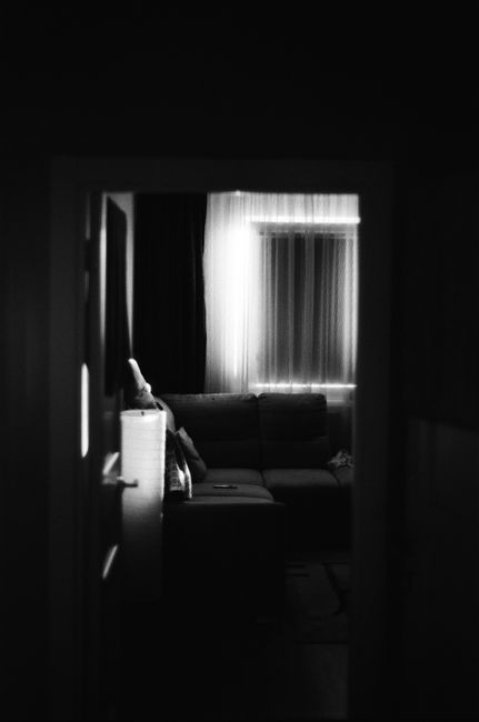 A moody black and white photo of a modern living room viewed through a doorway.