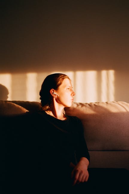 A contemplative woman sitting on a sofa basked in warm sunset light.