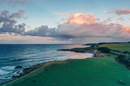 Breathtaking aerial view of a coastline with lush grassfields under a stunning sunset sky.
