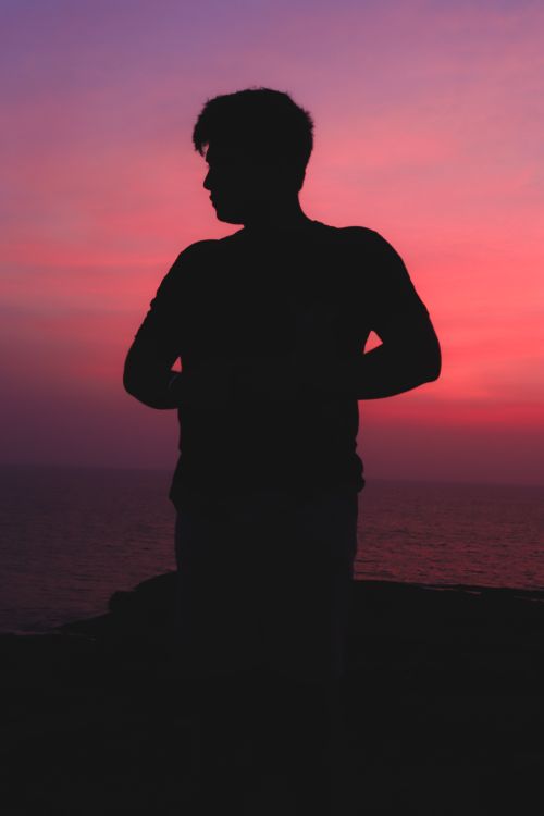 Free A silhouette of a man standing by the sea during a vibrant sunset. Stock Photo