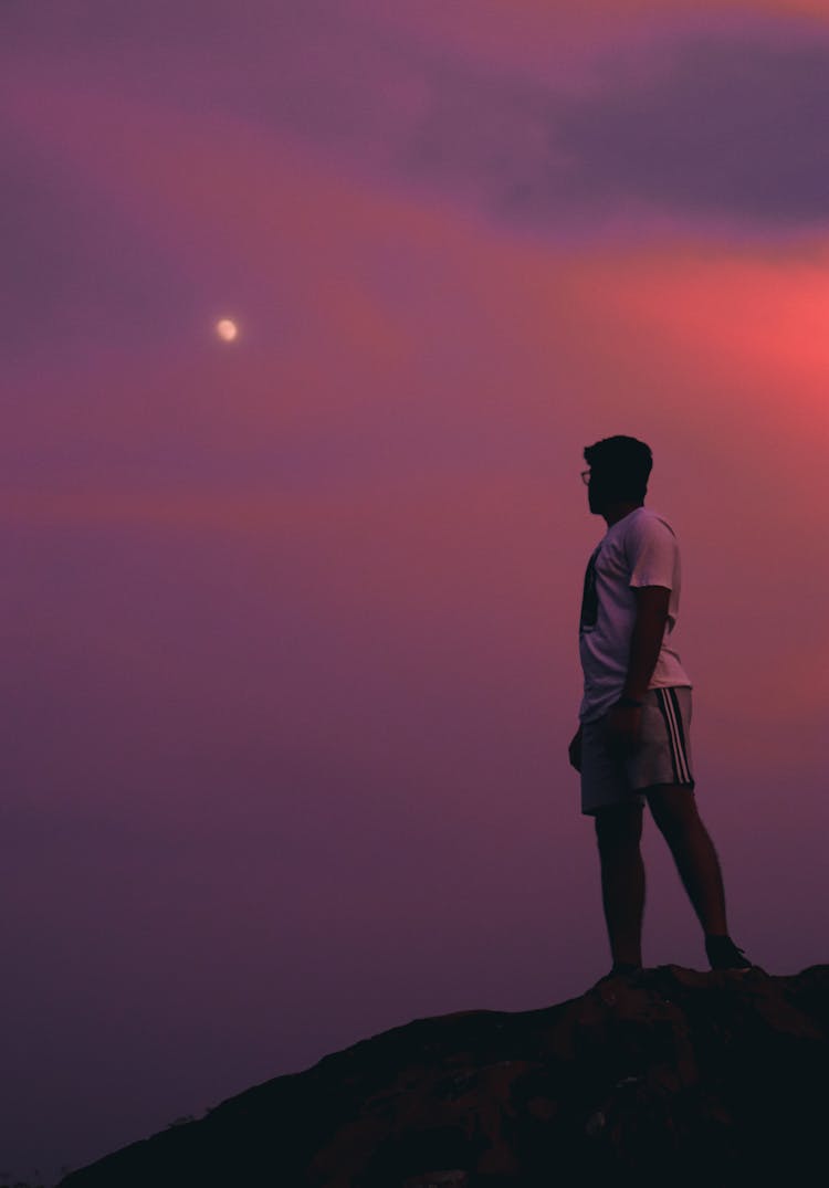 Man Standing On A Rock Formation Looking At The Moon 