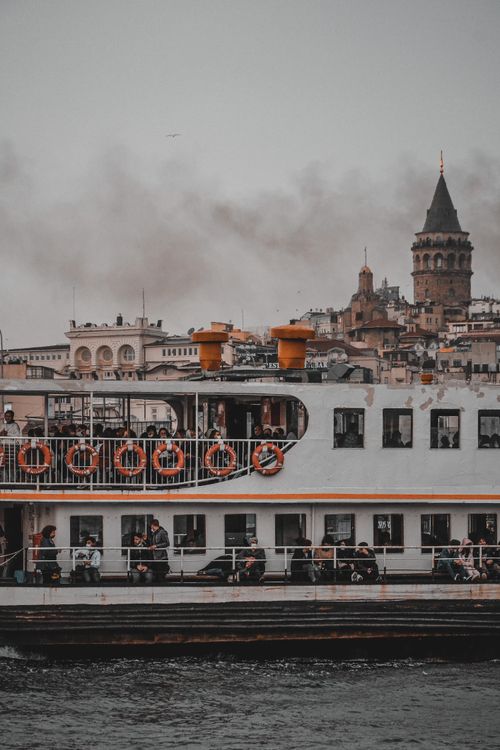 Free Scenic view of Galata Tower and ferry crossing the Bosphorus under an overcast sky in Istanbul, Turkey. Stock Photo
