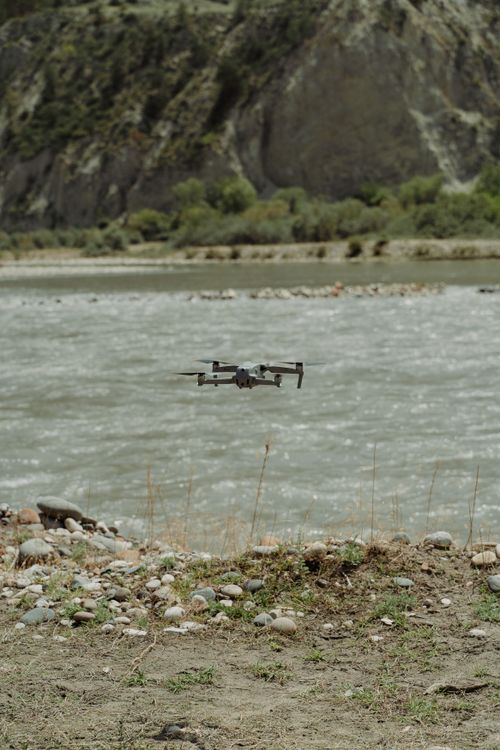 Free Drone captured flying over a serene river, surrounded by rocky terrain and lush greenery. Stock Photo