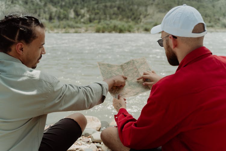 Men Looking At A Map While Sitting By The River