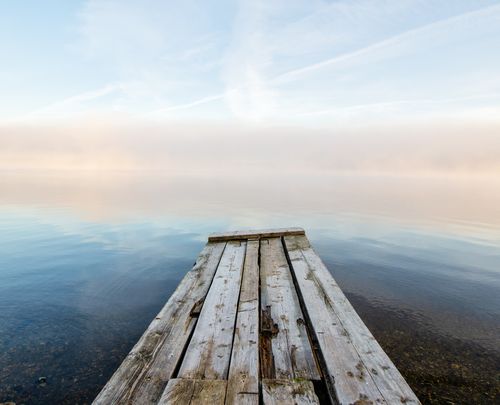 Free Tranquil scene of a weathered wooden pier extending into a serene lake under a pastel sky. Stock Photo