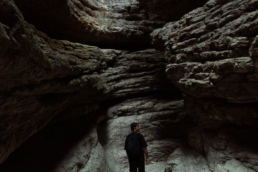 A man wearing a backpack explores a dimly lit cave with remarkable rock formations.