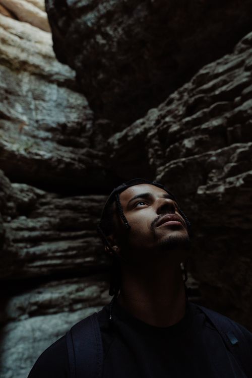 Free A man gazes upward in a dimly lit rocky cave, capturing a moment of introspection. Stock Photo