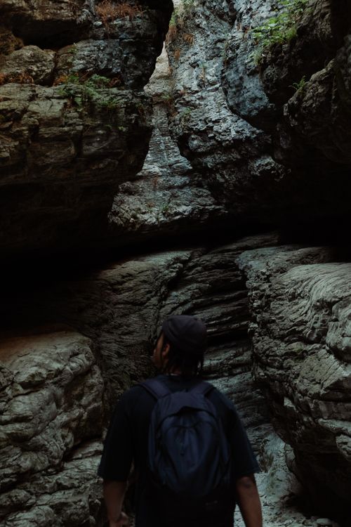 Free A person standing inside a rocky cave, wearing a backpack, and looking towards the light. Stock Photo