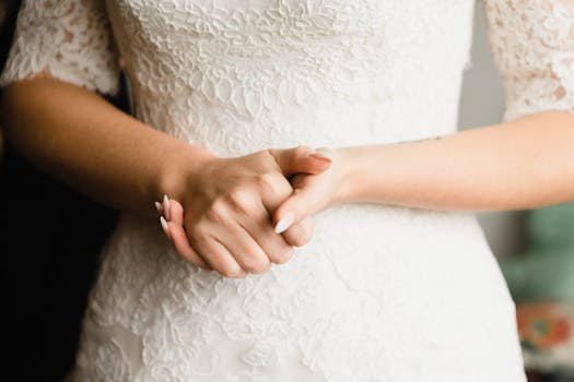 Close-up of bride's hands in lace wedding dress, conveying elegance and anticipation.
