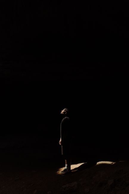 A person stands in a dark cave, illuminated by a ray of light, creating a mysterious atmosphere.