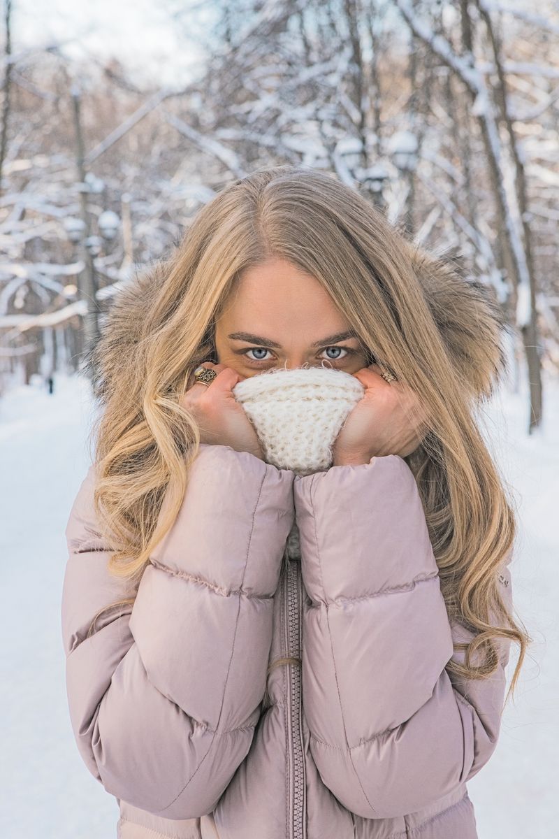 Woman in a pink puffer jacket and scarf in a snowy park