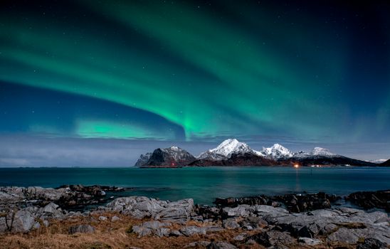 Captivating view of the Northern Lights dancing over snow-capped mountains and a tranquil body of water in Norway.
