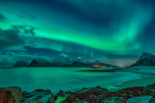 Stunning view of the aurora borealis illuminating the mountains and sea in Nordland, Norway.