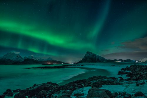 Free Stunning display of the Aurora Borealis illuminating the snow-covered coast and mountains in Nordland, Norway at night. Stock Photo