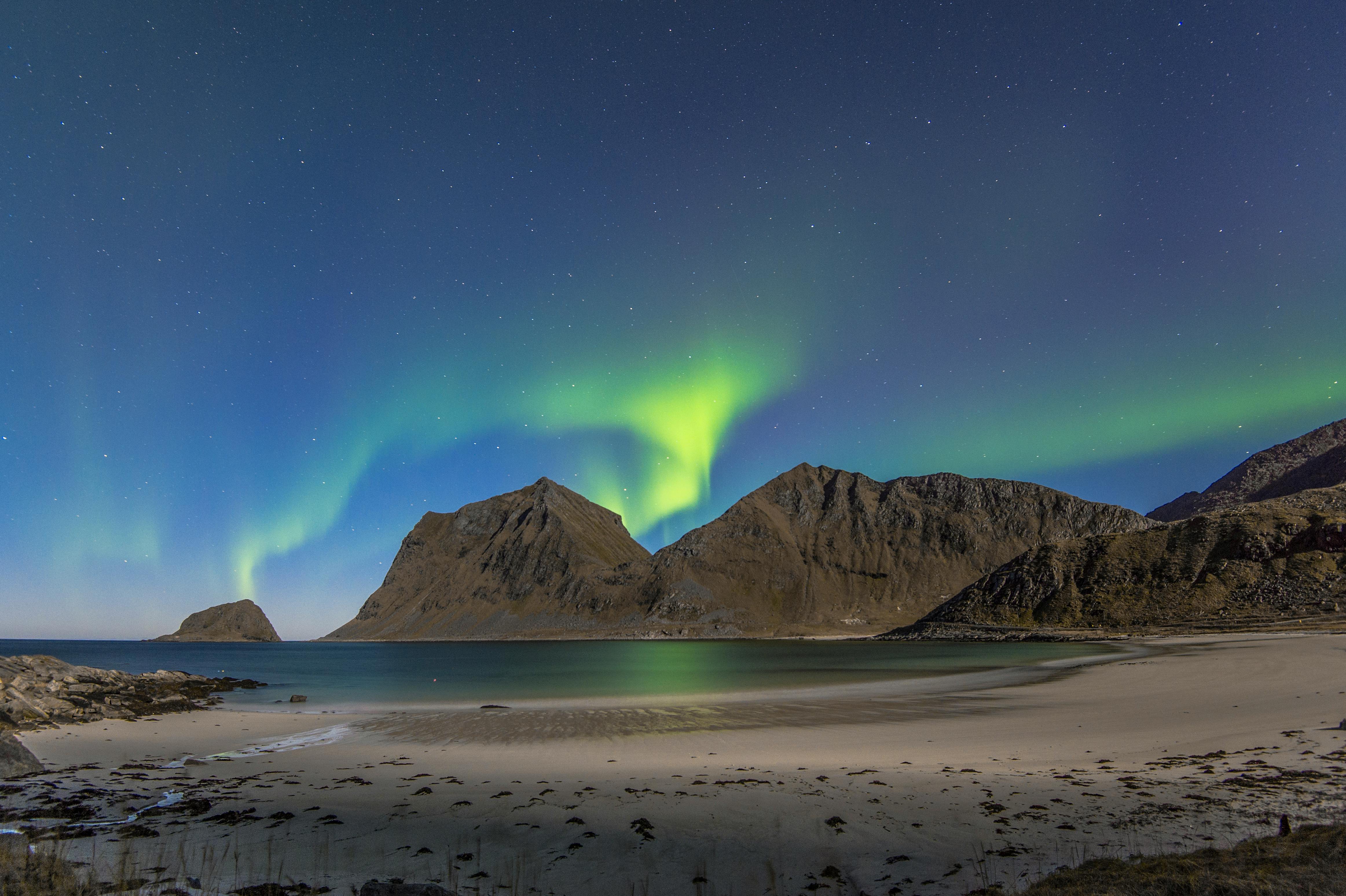 北极光照亮了挪威罗弗敦宁静海滩上的夜空，背景是雄伟的山脉