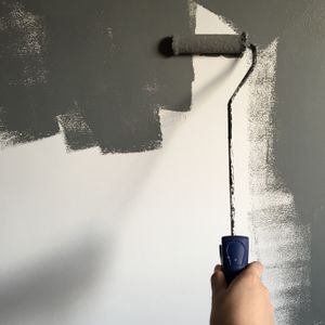 Hand rolling grey paint over a white wall