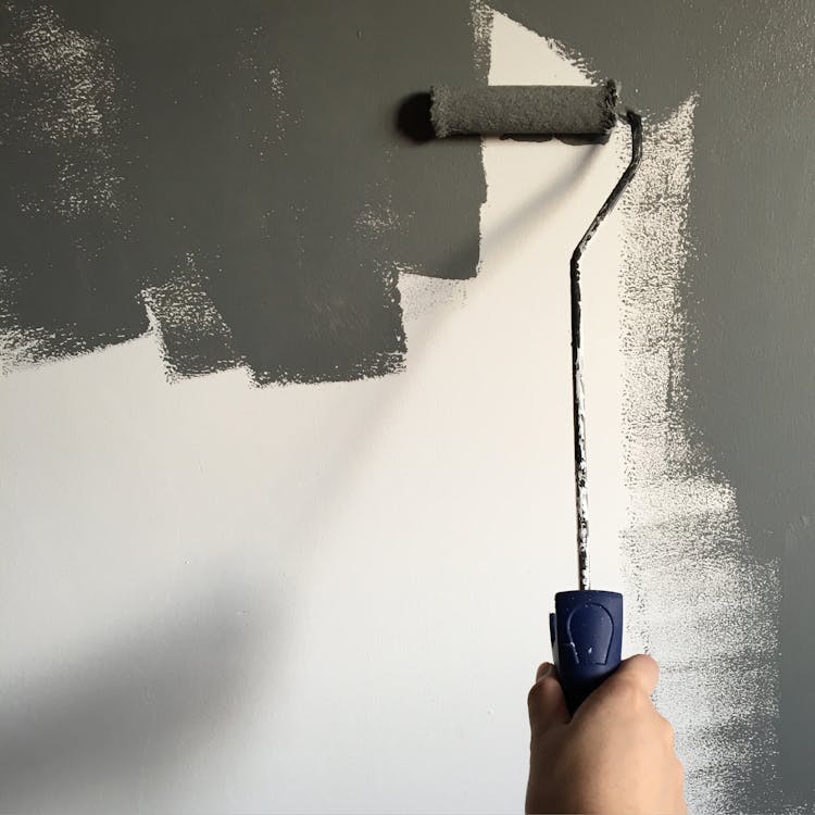 Person Holding Paint Roller While Painting The Wall