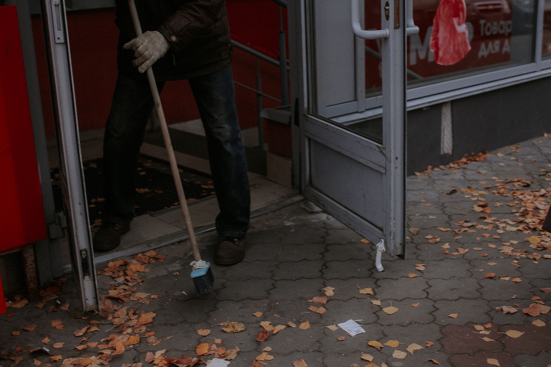 Person sweeping dry leaves outside a shop entrance during fall.