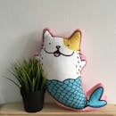 木架上的绿色植物旁边，放着一个可爱的猫-美人鱼毛绒玩具