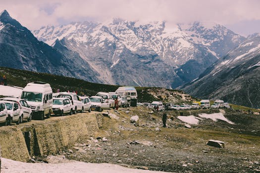 Vehicles lined up on a snowy mountain road, surrounded by majestic peaks and clear sky.