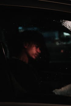 Side view of a man sitting in a car with rain on the window, creating a moody atmosphere.