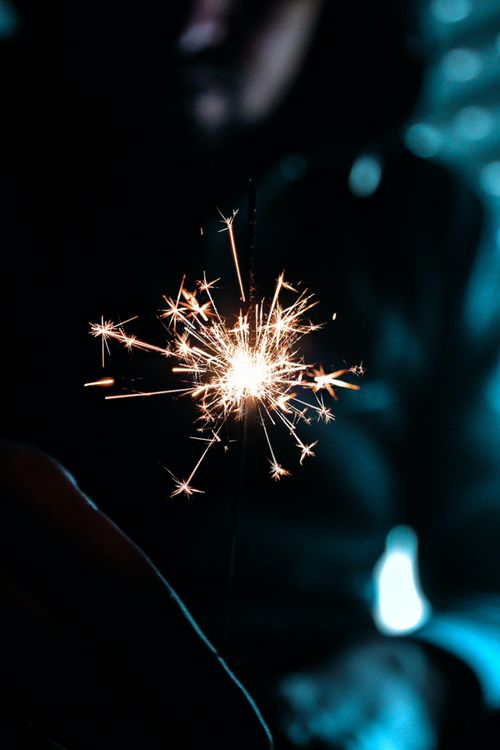 Free A bright sparkler crackling in the foreground against a mysterious dark background. Stock Photo