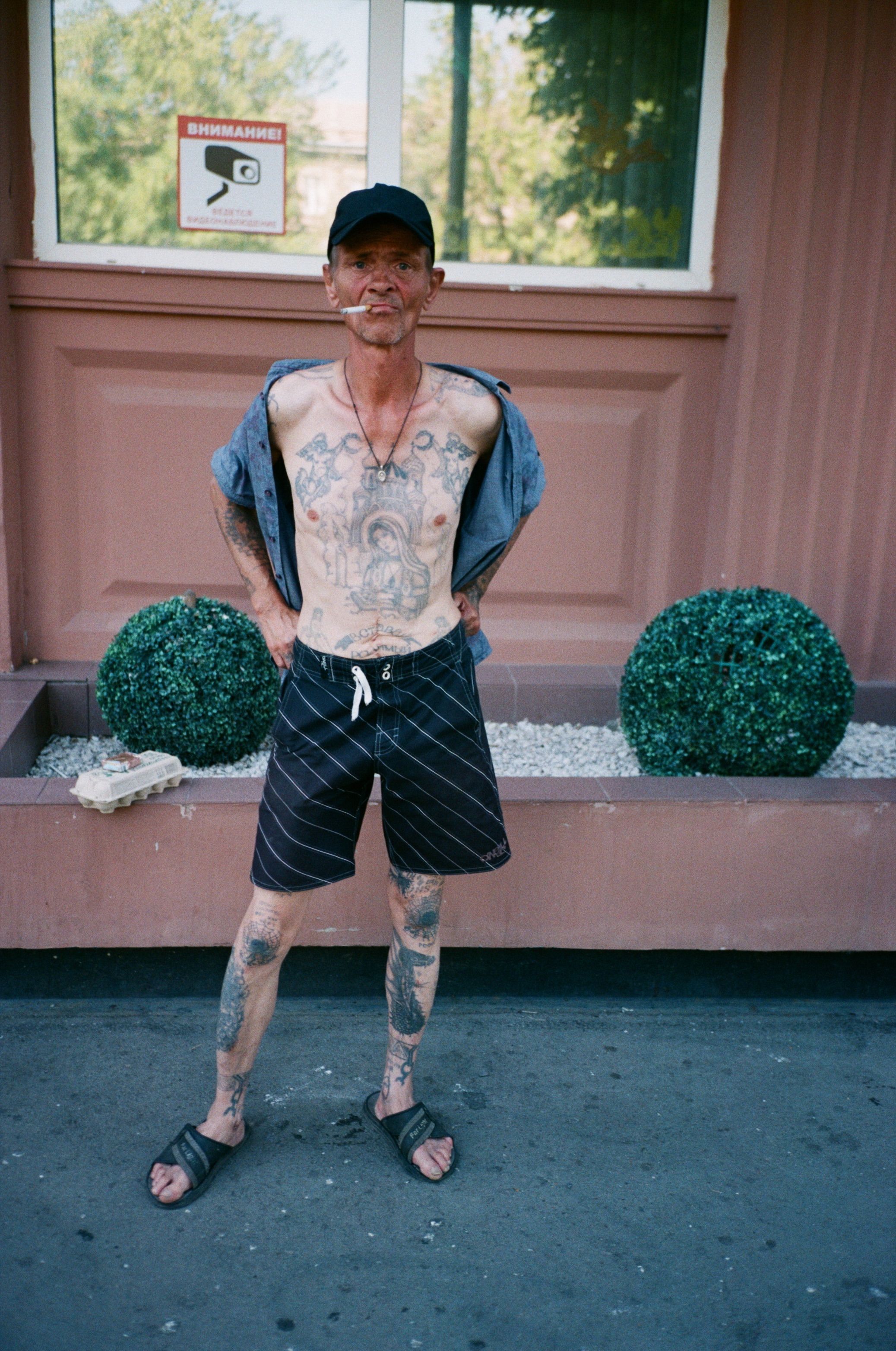 A tattooed man in shorts stands confidently outside an urban building during the day.
