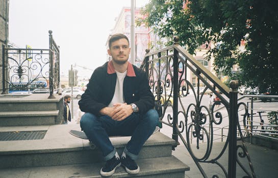 Casual young man sitting on city stairs with a skateboard, enjoying the urban street view.