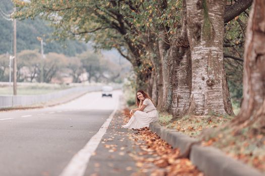 A Female Sitting on Curb Next to a Road 