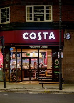 A Costa Coffee shop illuminated at night in an urban area, showcasing its welcoming atmosphere.