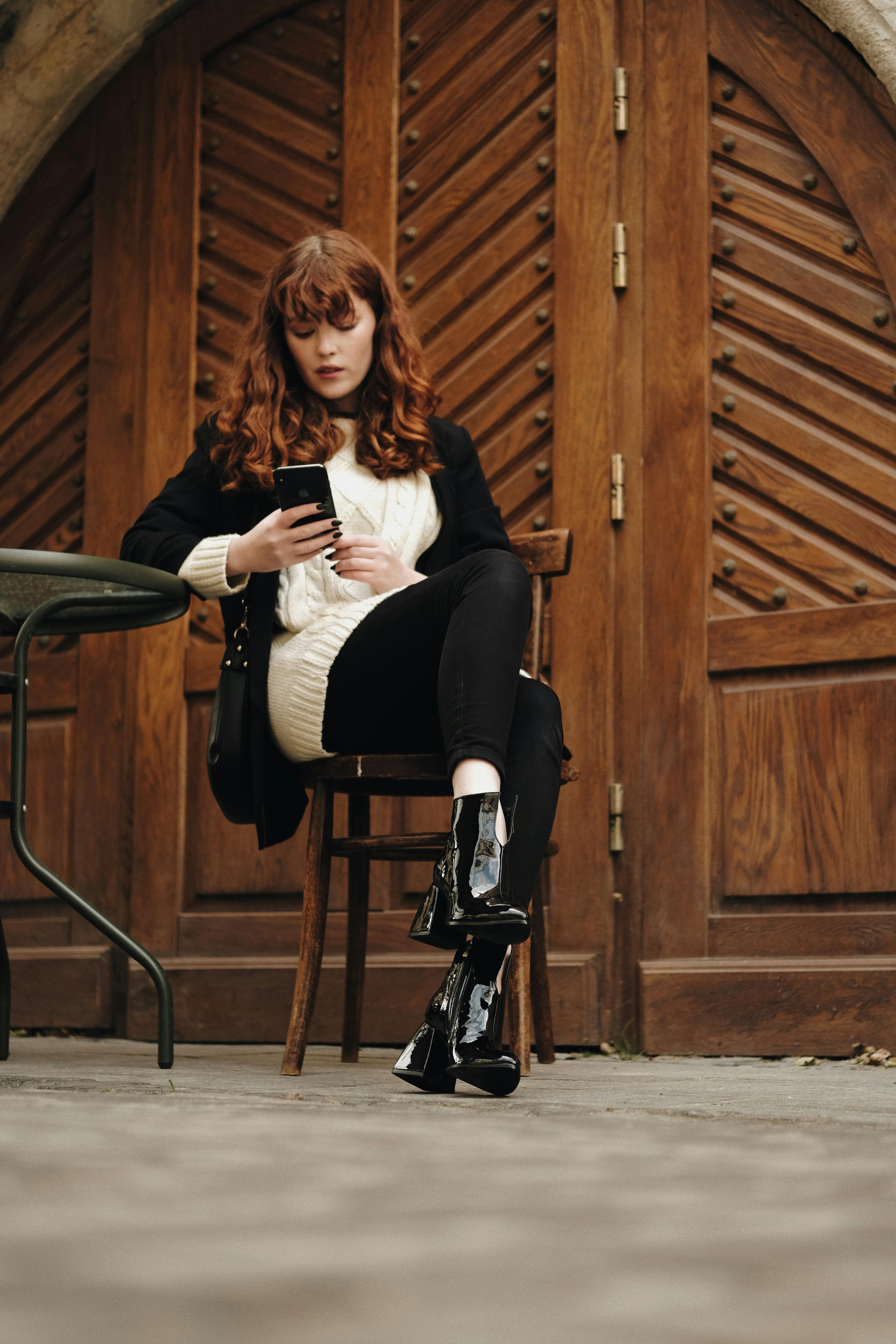 Stylish woman in black and white attire using a smartphone while sitting outdoors.