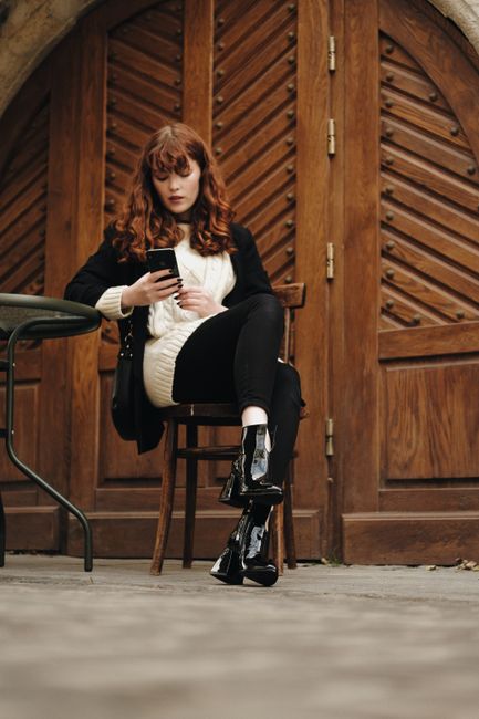 Stylish woman in black and white attire using a smartphone while sitting outdoors.