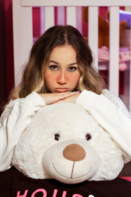Woman Wearing a White Top Resting Face on Hands on a Stuffed Toy