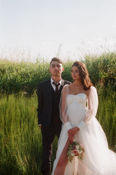 A romantic wedding portrait featuring a bride and groom standing in a lush grassfield, captured in natural light.
