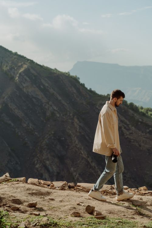 Free A man walks along a mountain trail holding a camera. Scenic background of rugged mountains. Stock Photo
