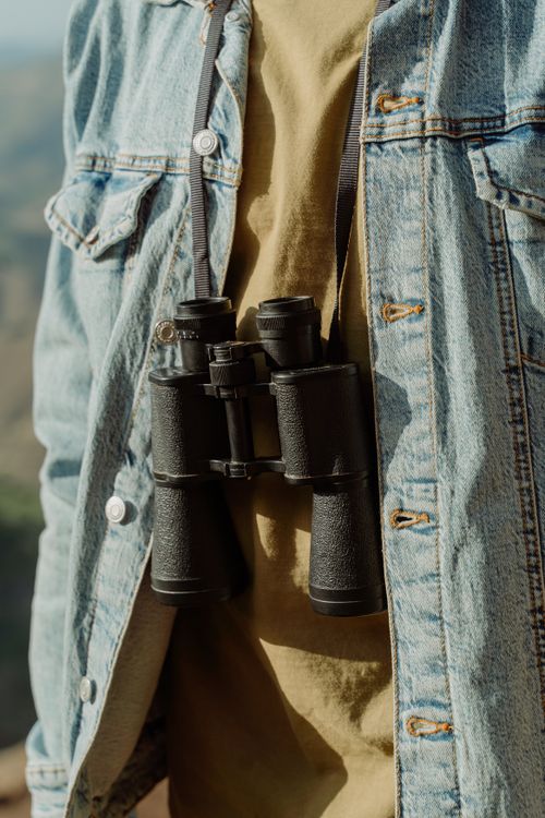 Free Close-up of a hiker wearing a denim jacket with binoculars on an outdoor adventure. Stock Photo