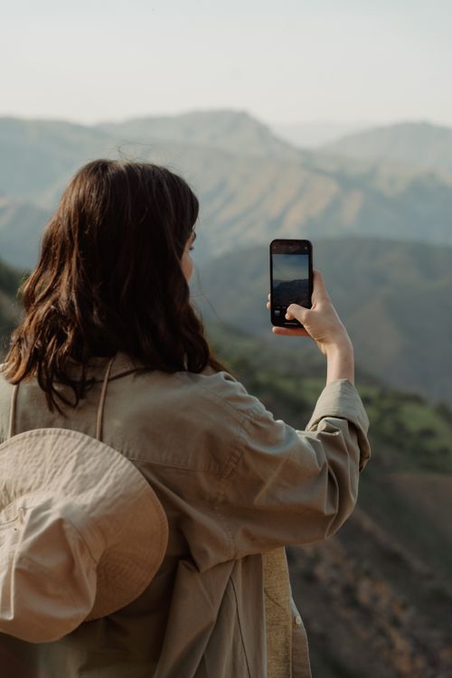 Free Woman taking a photo with smartphone, capturing beautiful mountain scenery during daytime. Stock Photo